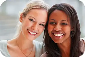 Two smiling women leaning their heads together.