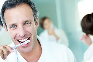 Smiling man brushing his teeth in the bathroom.